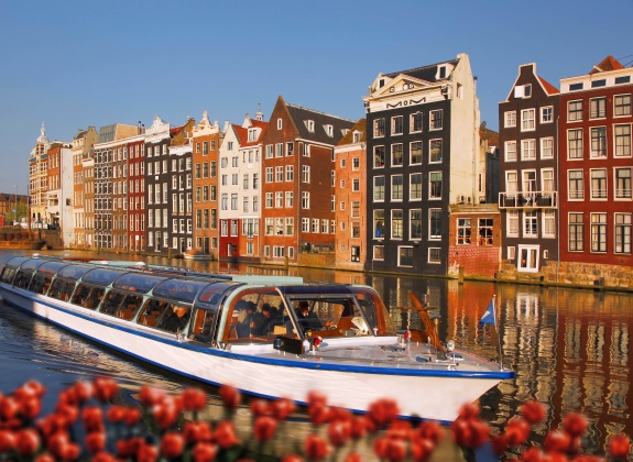Amsterdam city with boats on canal against red tulips in Holland