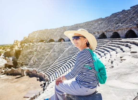 Mature beautiful woman traveler, sits on the steps of the amphitheater in admiring the view