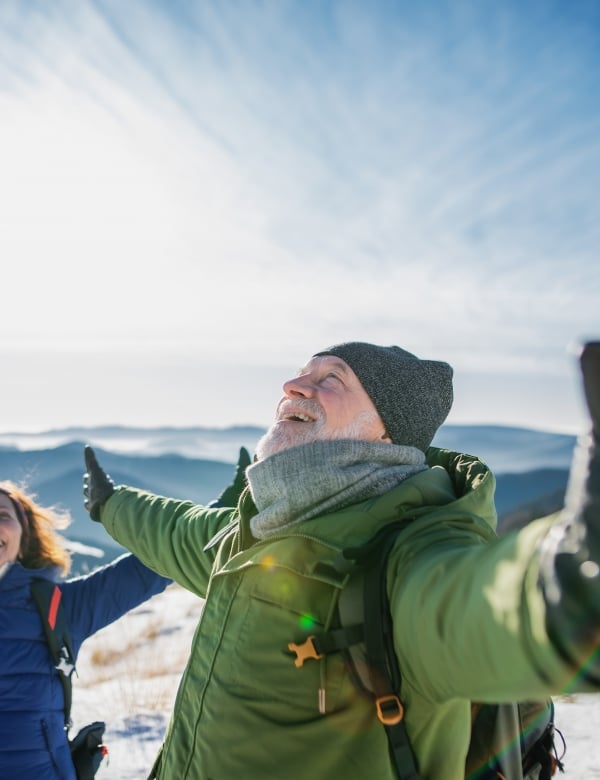 Senior couple hikers in snow-covered winter nature, stretching arms.
