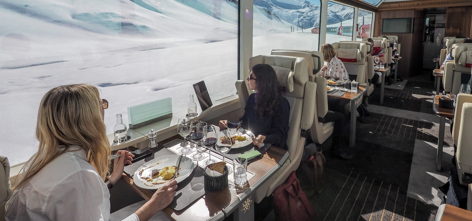 Onboard the Glacier Express - Excellence Class Train travellers look out of the window and the snowy Alpine scenery