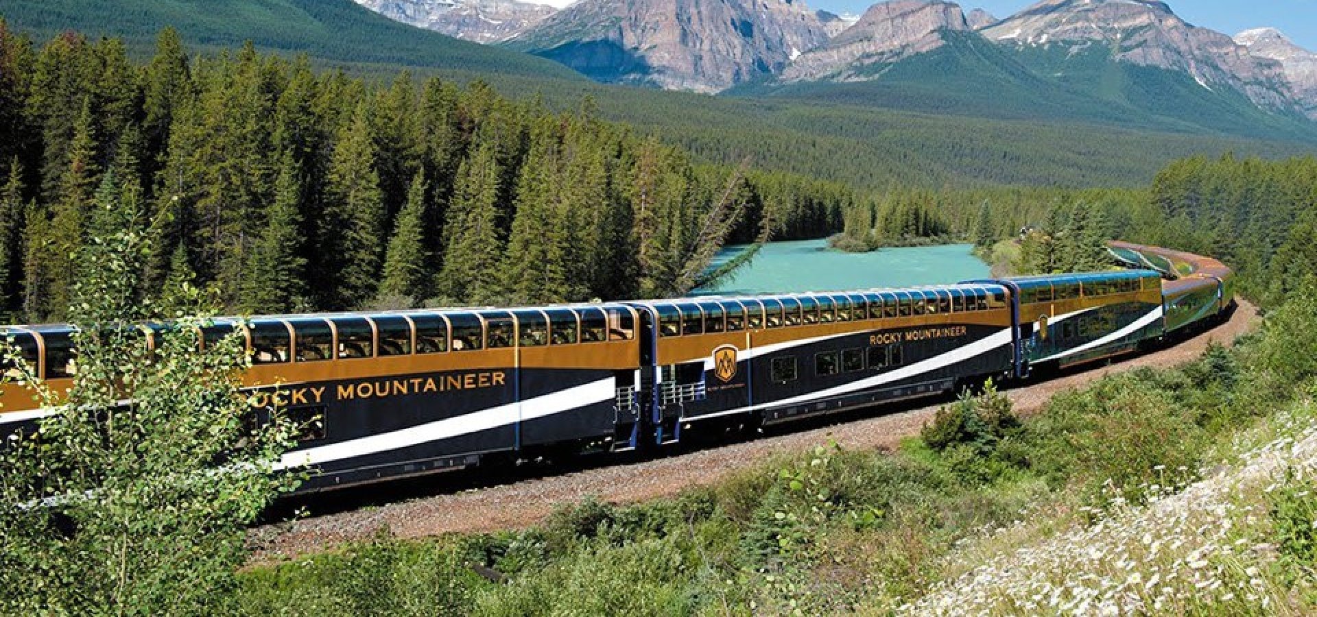 Rocky Mountaineer Navy blue and Gold train carriages on the track passing lake