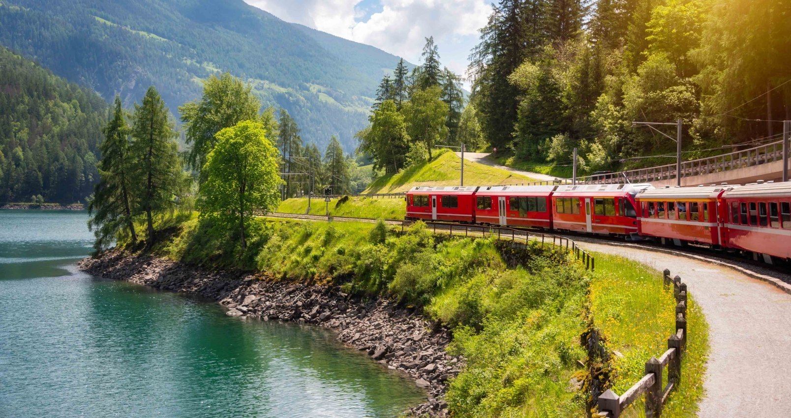 Red train moving along lake in beautiful mountain landscape in Switzerland