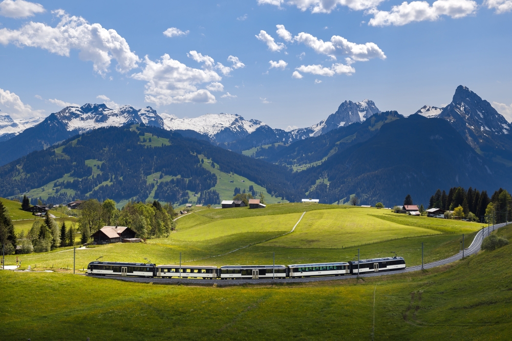 The GoldenPass route A train travels through a valley with high mountains in the background