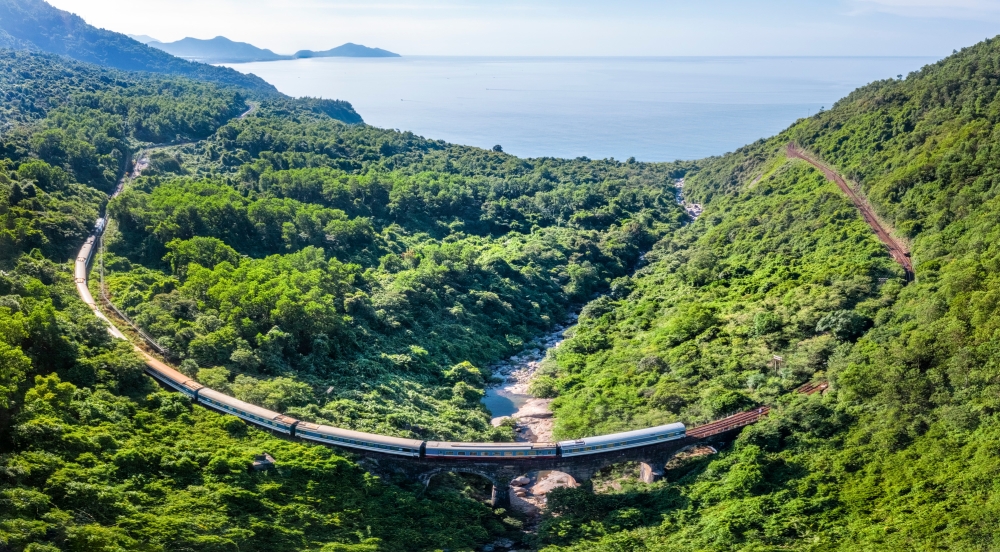 A train travels through lush landscape with coast on horizon